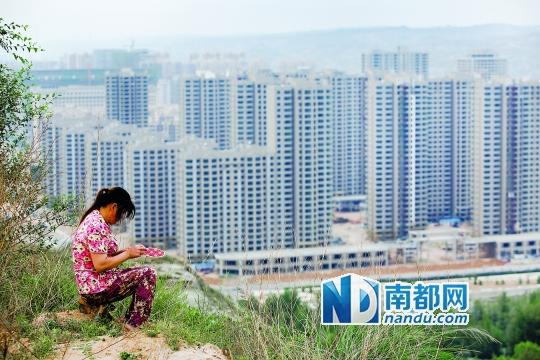 神木新村西面的山坡上，一名磚窯的員工坐在坡頂繡鞋墊。席卷神木的民間借貸危機壓垮了當(dāng)?shù)貥鞘幸惨l(fā)債務(wù)危機，高樓林立的神木新村今年大部分工程已經(jīng)停工。南都記者孫俊彬攝